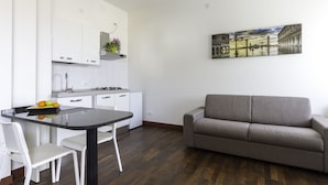 A modern kitchen with white cabinets, a dining table, and a gray sofa.