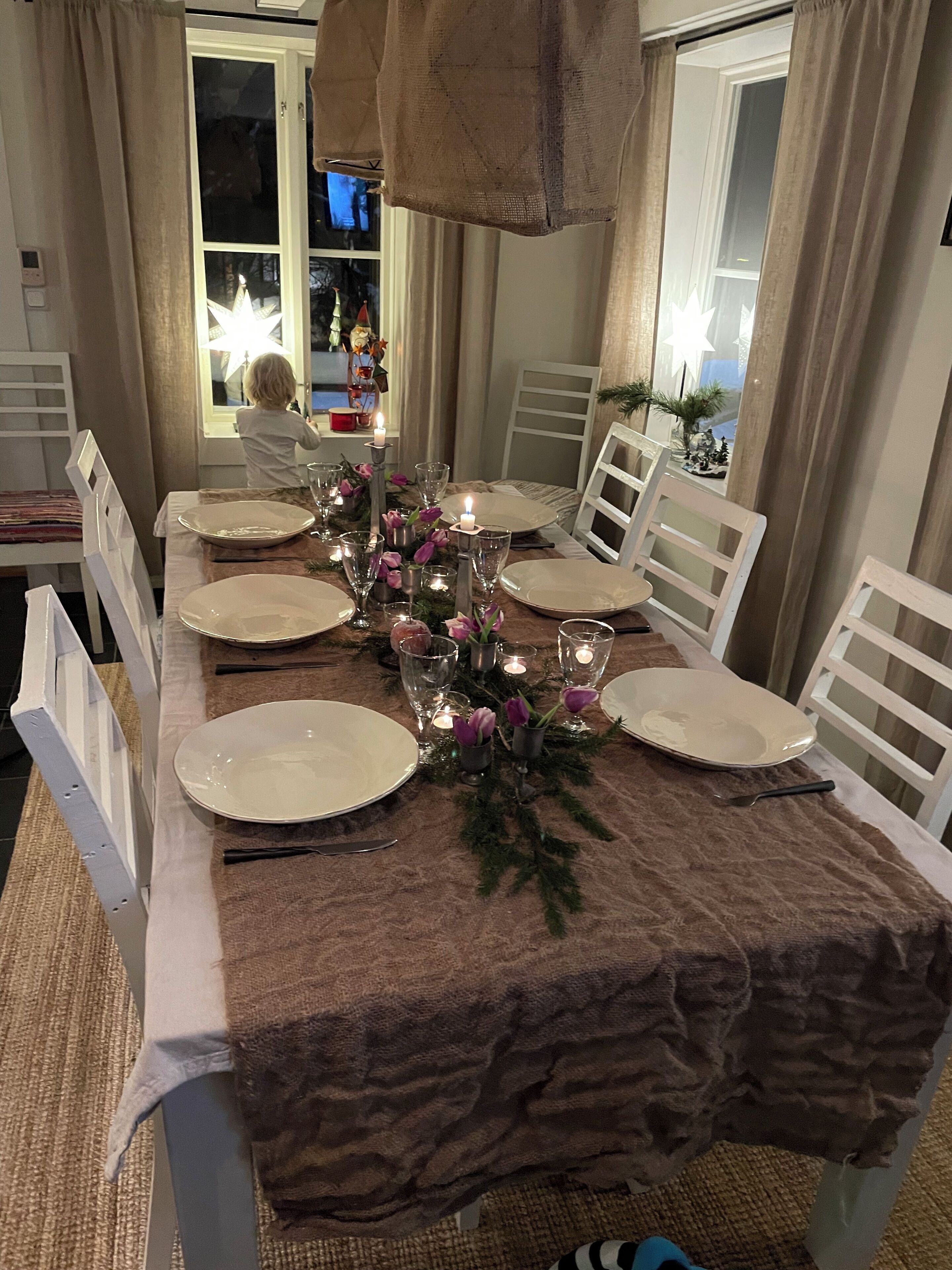 Taula de dinar preparada amb plats, gots i espelmes, envoltada de cadires blanques.