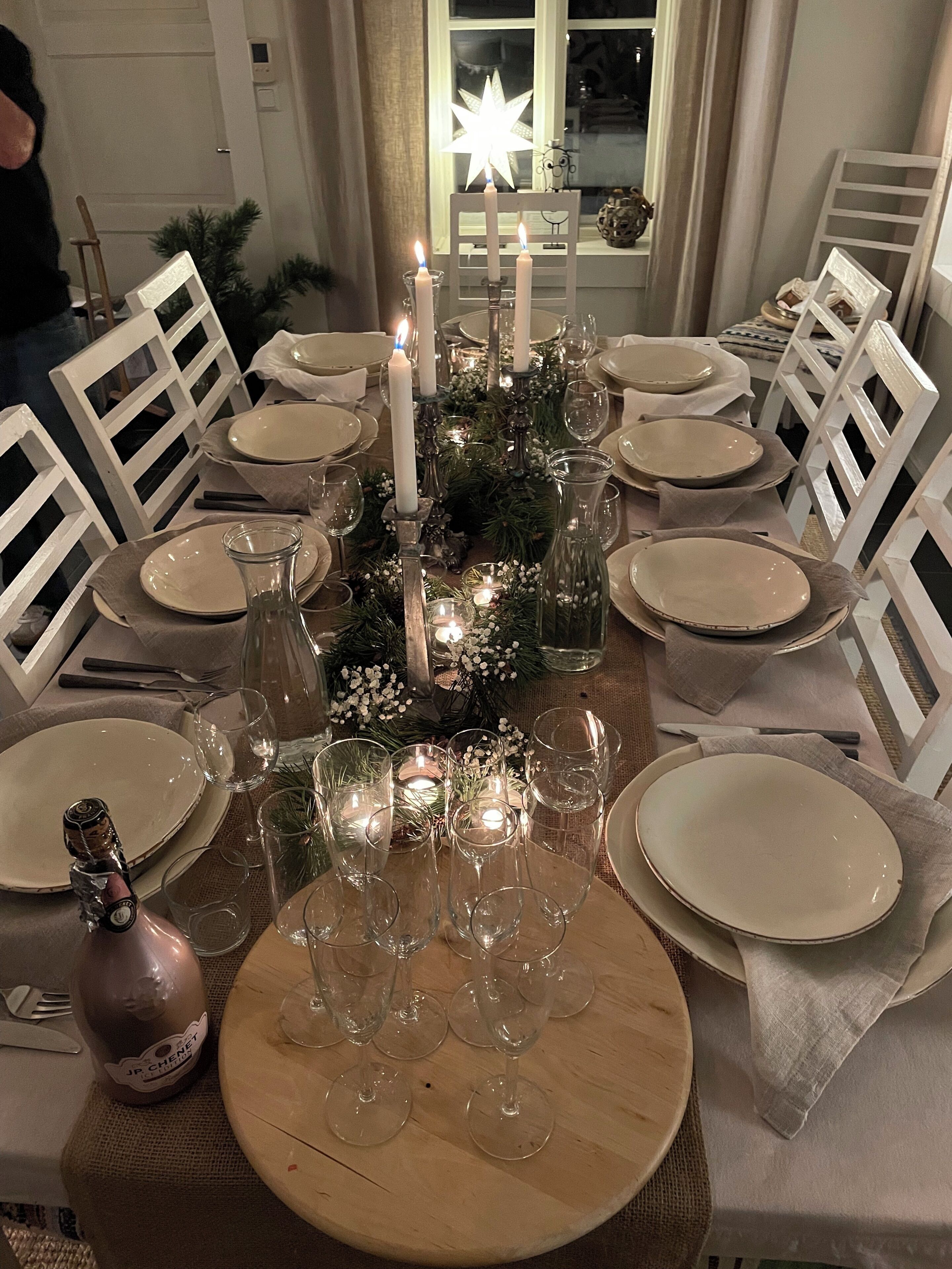 Tavola da pranzo imbandita per sei persone, con sedie bianche, candele e un lampadario a forma di stella.