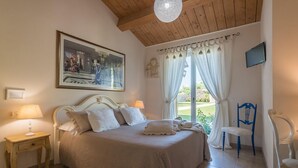 A bedroom with a bed, two bedside tables, a painting, a window with curtains, a chair, and a television. - Casa Emanuela - Private villa, 4 bedrooms, pool, A/C, wifi, pets, Marche (Fermignano)