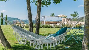 A hammock set up between trees in a grassy area with a view of a building and mountains in the background.
