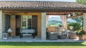 A covered outdoor area with a foosball table, wicker furniture, and a view of the countryside.