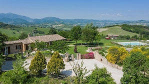 A villa with a tiled roof, a swimming pool, and a view of rolling hills and mountains.