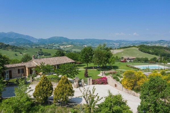 Eine Villa mit einem Ziegeldach, einem Swimmingpool und Blick auf sanfte Hügel und Berge.