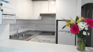 A modern kitchen with white cabinets, a stainless steel sink, and a built-in oven. There is a vase with flowers on the counter. - AIR CONDITIONING, FREE WIFI, NE TFLIX, ONLY 2 MINUTES BEACH (Alicante)
