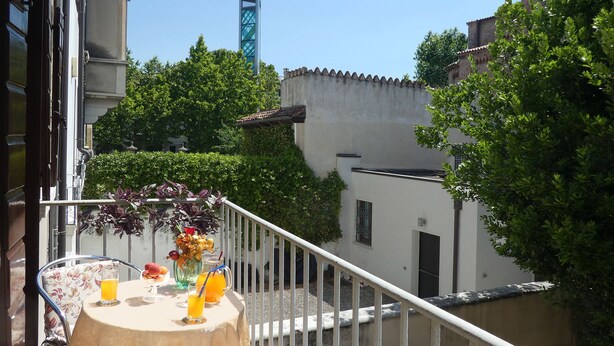 Een balkon met een ronde tafel, twee stoelen, een vaas met bloemen en twee glaasjes sinaasappelsap.
