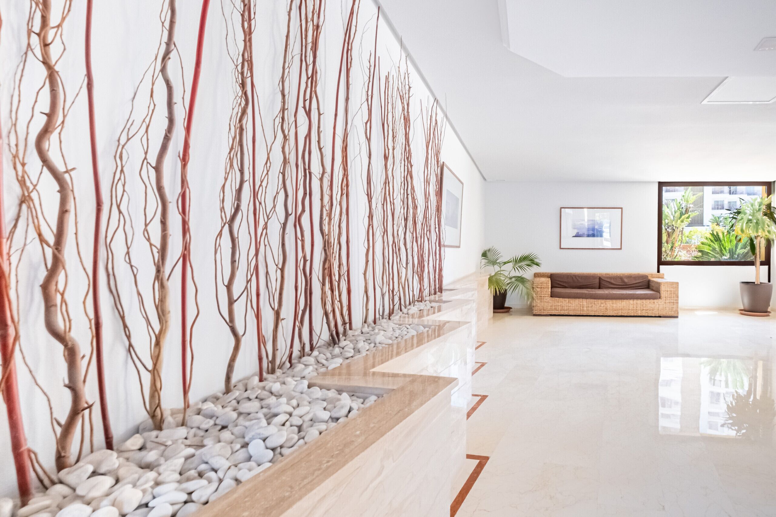 Um lobby moderno com um balcão de recepção extenso, um sofá e uma grande janela com plantas.