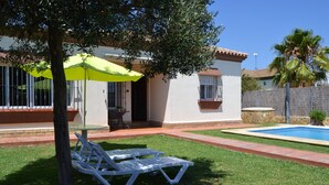 A house with a swimming pool, a lawn, and a patio area with a table and chairs. - Villa with private pool in Pinar de los Franceses (WIFI) (Chiclana De La Frontera)