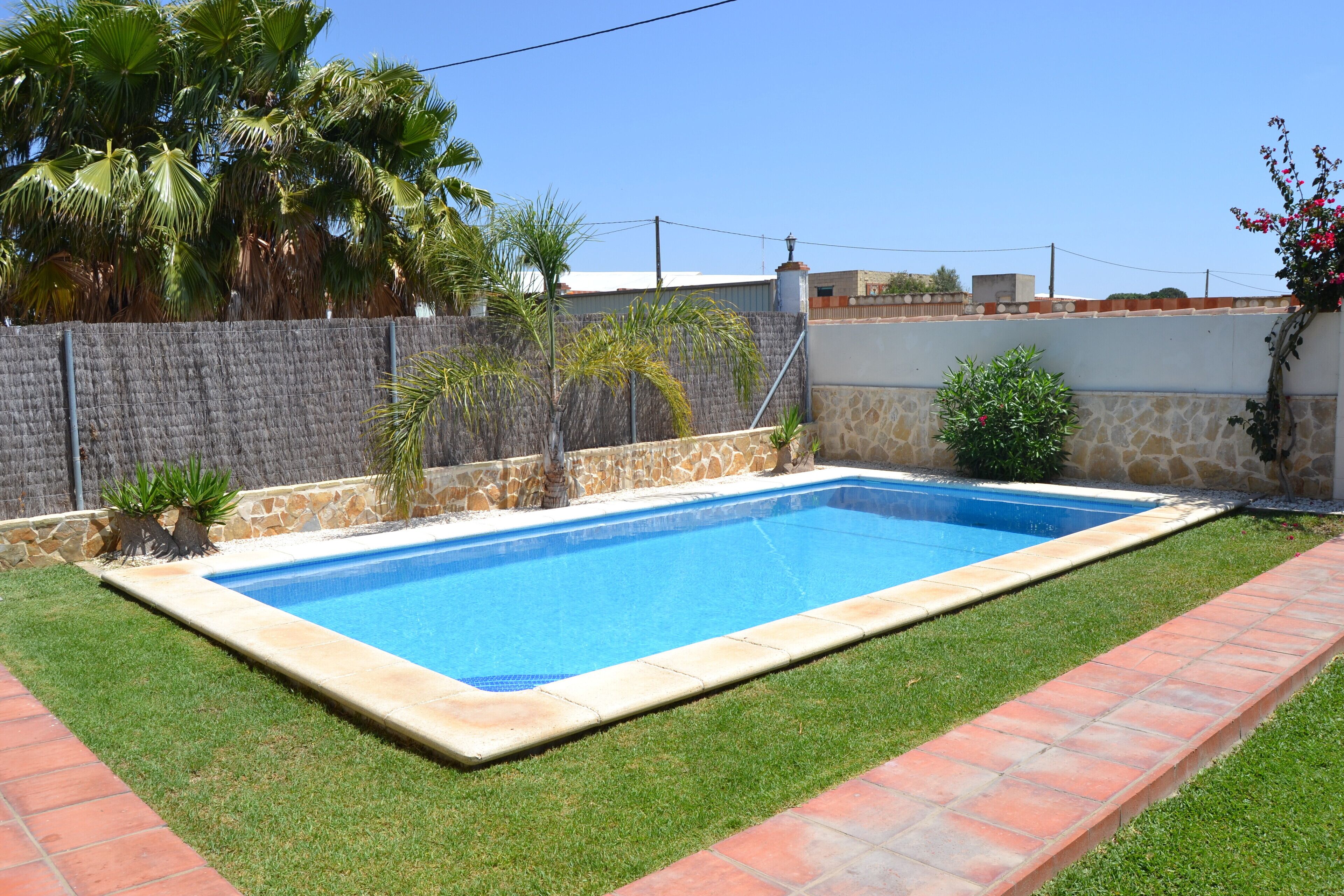 A rectangular swimming pool with a stone wall and a grassy area with a brick pathway.