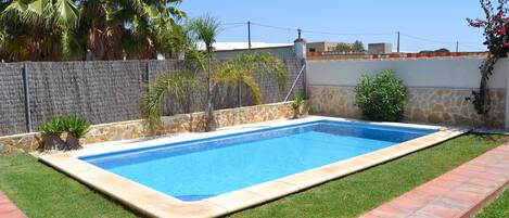 A rectangular swimming pool with a stone wall and a grassy area with a brick pathway.