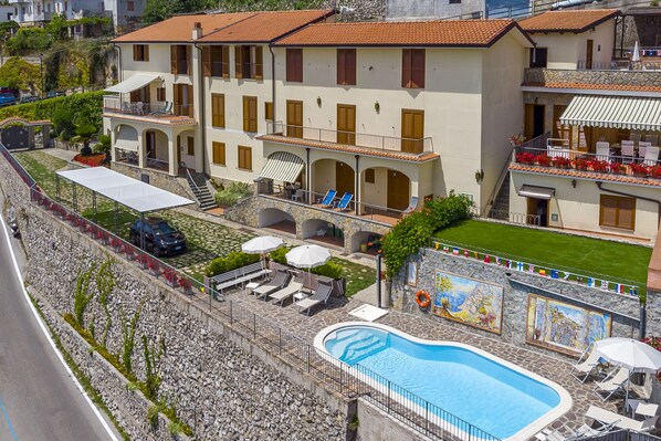 A multi-story building with a swimming pool, outdoor seating, and a stone wall with flags. - Apt Emma in Villa Laura near Ravello (scala)