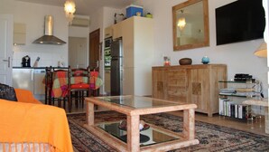 A living room with a glass-top coffee table, a dining area with chairs and a table, a kitchen with appliances, and a large mirror on the wall. - Apartment/ flat - LUMIO (Lumio)
