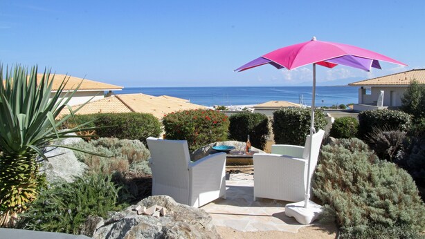 A patio with white wicker furniture, a pink umbrella, and a view of the sea. - Apartment/ flat - LUMIO (Lumio)