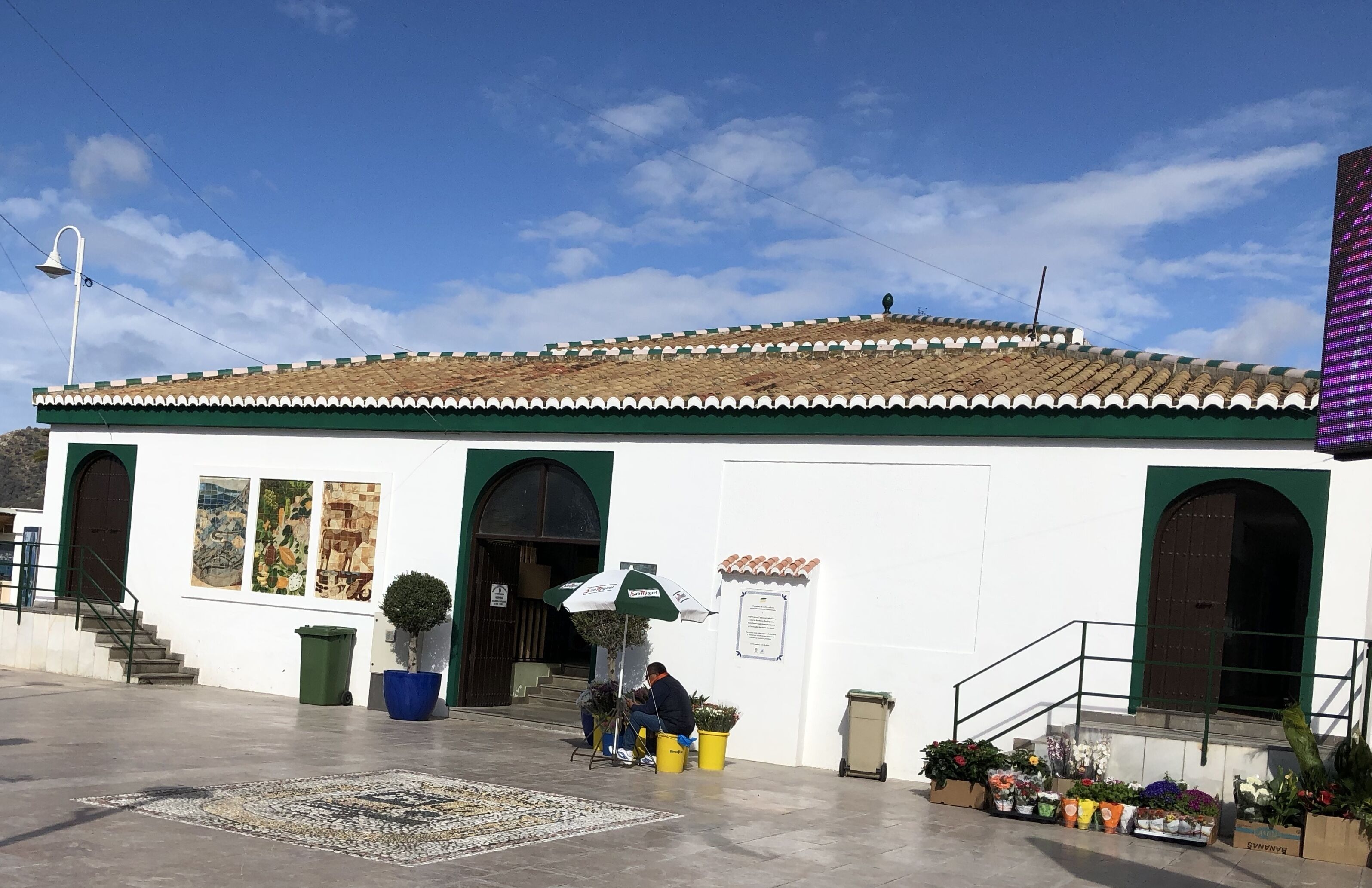 Un bâtiment avec un toit recouvert de tuiles, un auvent vert et une enseigne indiquant qu’il s’agit d’un commerce.