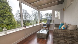 A sunroom with a view of trees, a wicker sofa, a chair, and a small table.