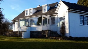 A white house with a large bay window, stone steps, and a stone wall.