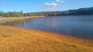 Um lago tranquilo com margens rochosas e uma colina arborizada ao fundo.