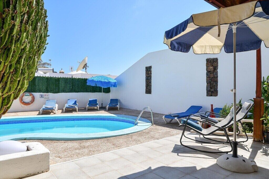A pool area with a clear blue pool, sun loungers, and umbrellas.