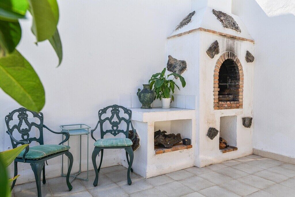 A patio with two green metal chairs, a small table, a potted plant, and a stone-built outdoor oven.