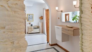 A hallway with a white tiled floor, a wooden door, a white dresser, and a mirror with wall sconces. - Villa with private pool and free wifi (Tías)