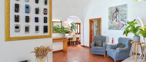 A spacious living area with a dining area, a framed collection of mobile phones on the wall, and a painting on the wall.