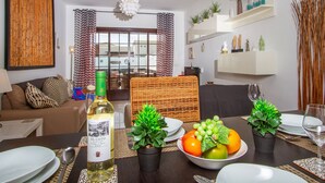 Un coin repas avec une table dressée pour deux personnes, une bouteille de vin et un saladier de fruits.