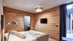 Ein modernes Schlafzimmer mit einer Holzwand, einem Bett mit weißen Bettwäsche, einer Nachttischlampe und einem an der Wand befestigten Flachbildfernseher.
