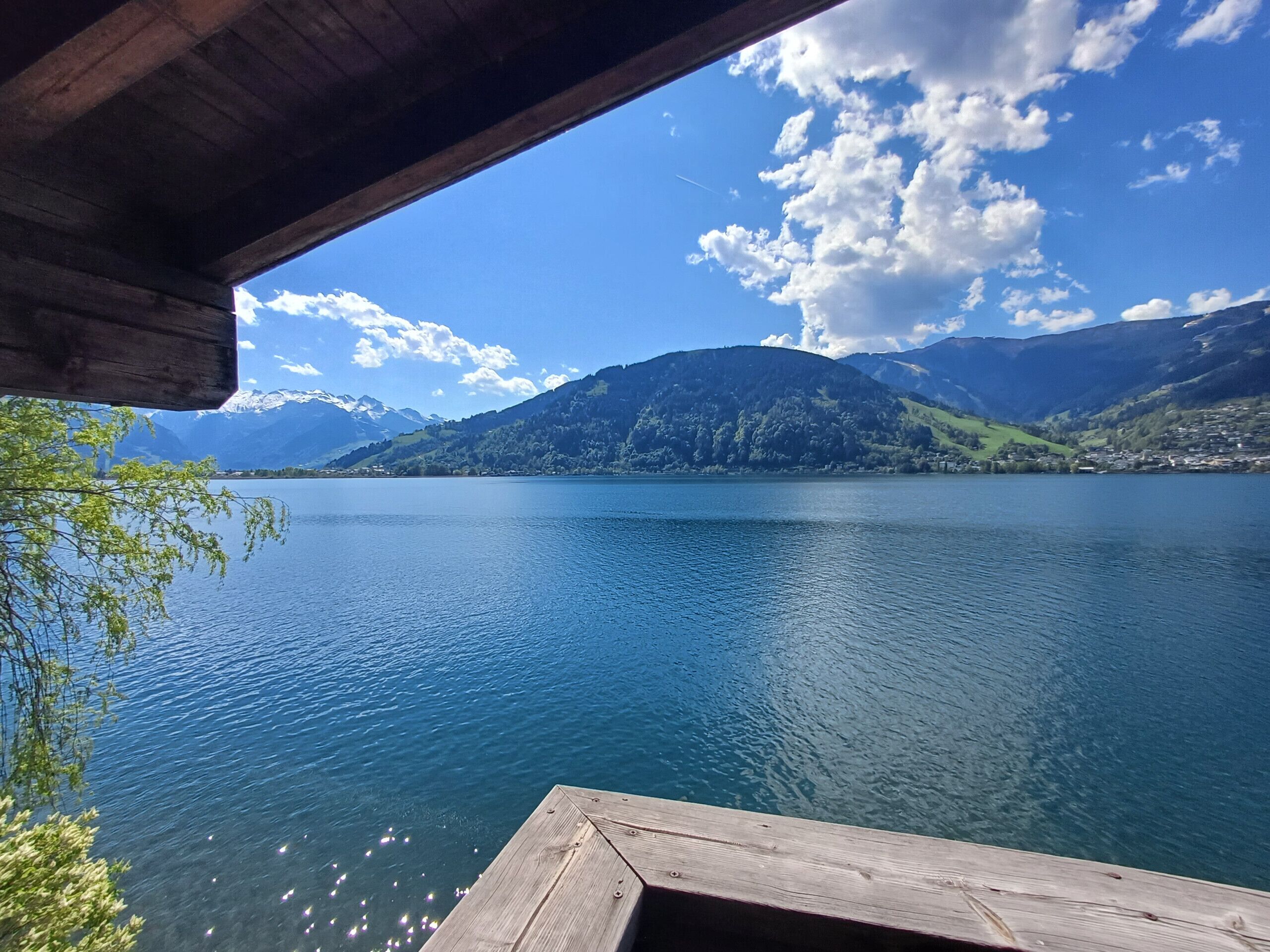 Um deck de madeira com vista para um lago calmo, com montanhas ao fundo.