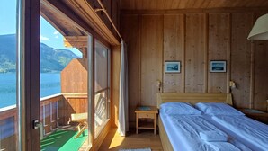 A wooden cabin room with a bed, a small table, and a view of a lake. - Waterfront Apartment 3 (Zell am See)