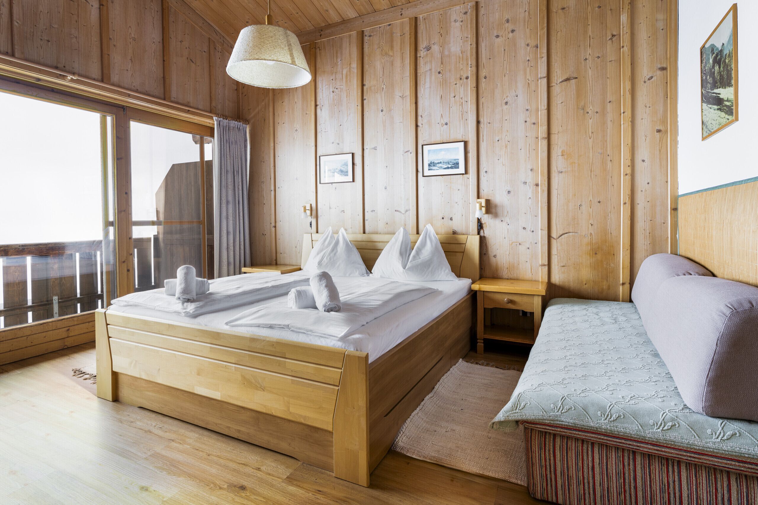Une chambre à coucher en bois, avec un lit, un canapé et une grande fenêtre.