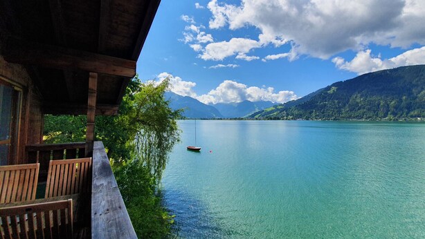 A wooden deck with chairs overlooking a calm lake with a boat, surrounded by mountains and clear skies. - Waterfront Apartment 3 (Zell am See)