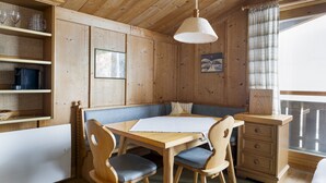 A wooden cabin interior with a dining table, chairs, a bench, a hanging light fixture, and a window with curtains. - Waterfront Apartment 3 (Zell am See)