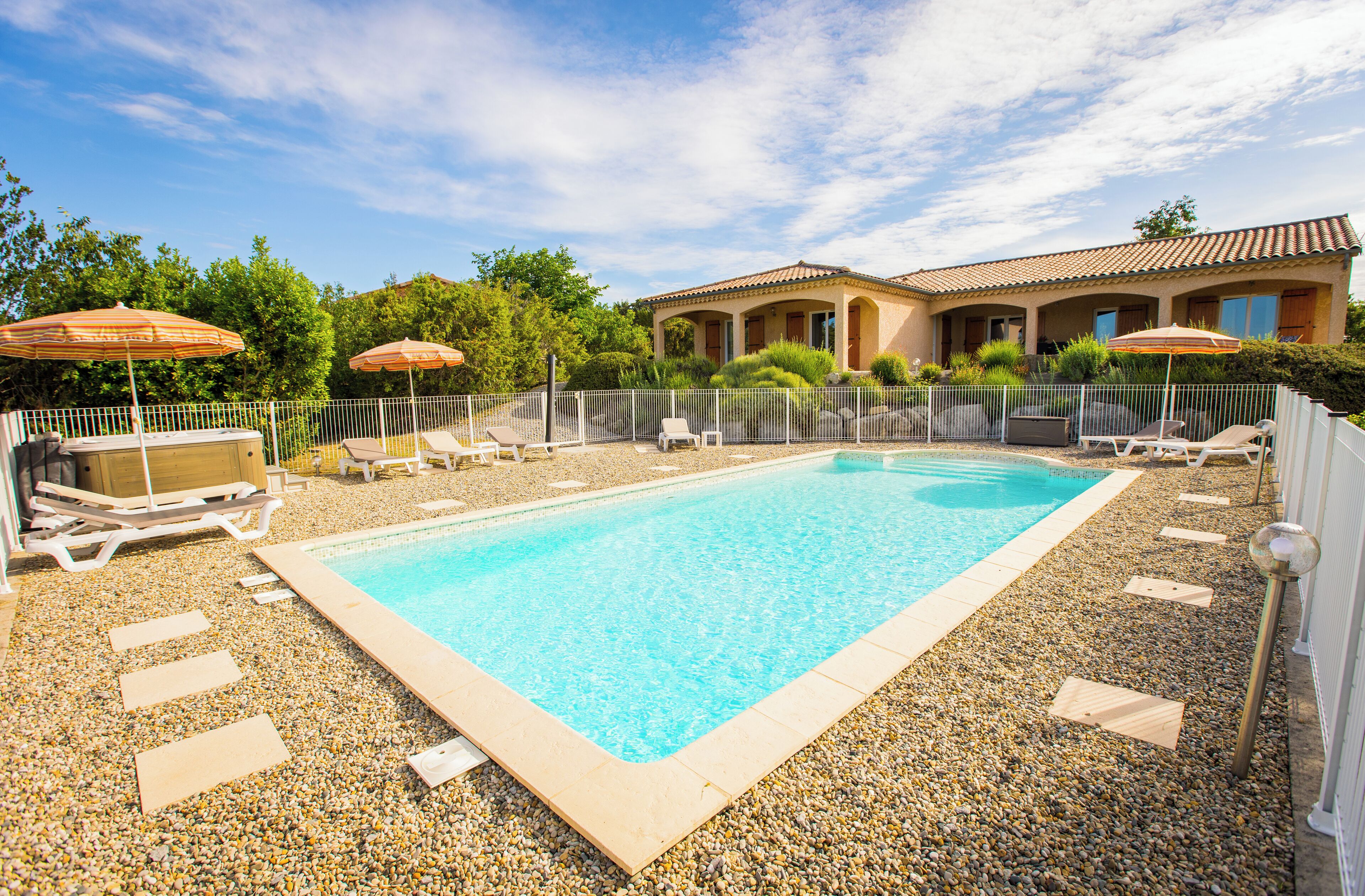 A rectangular swimming pool surrounded by a gravel area with lounge chairs and umbrellas.