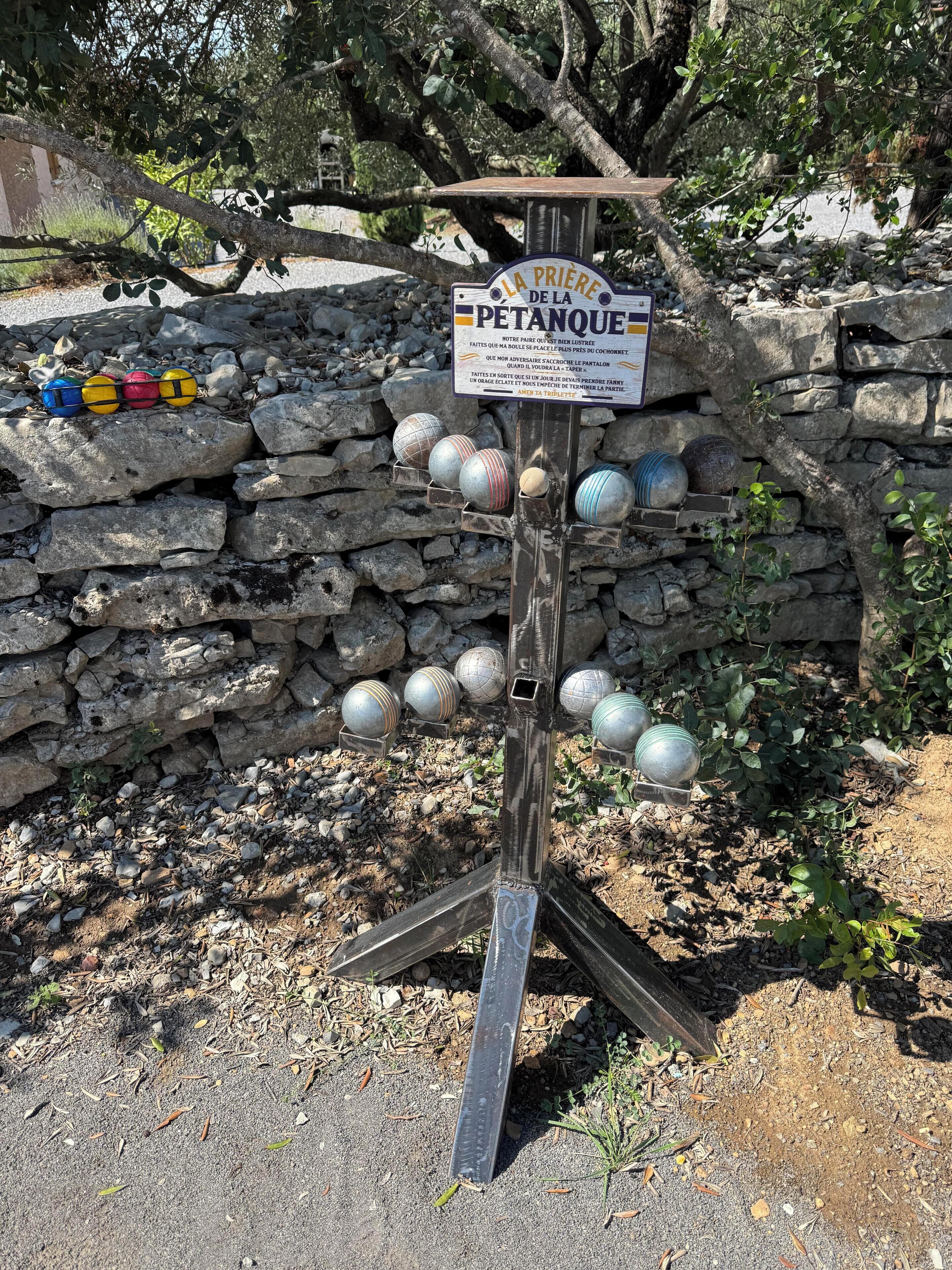 Un mur de pierre sur lequel est fixée une plaque, et un support métallique qui maintient plusieurs objets sphériques.