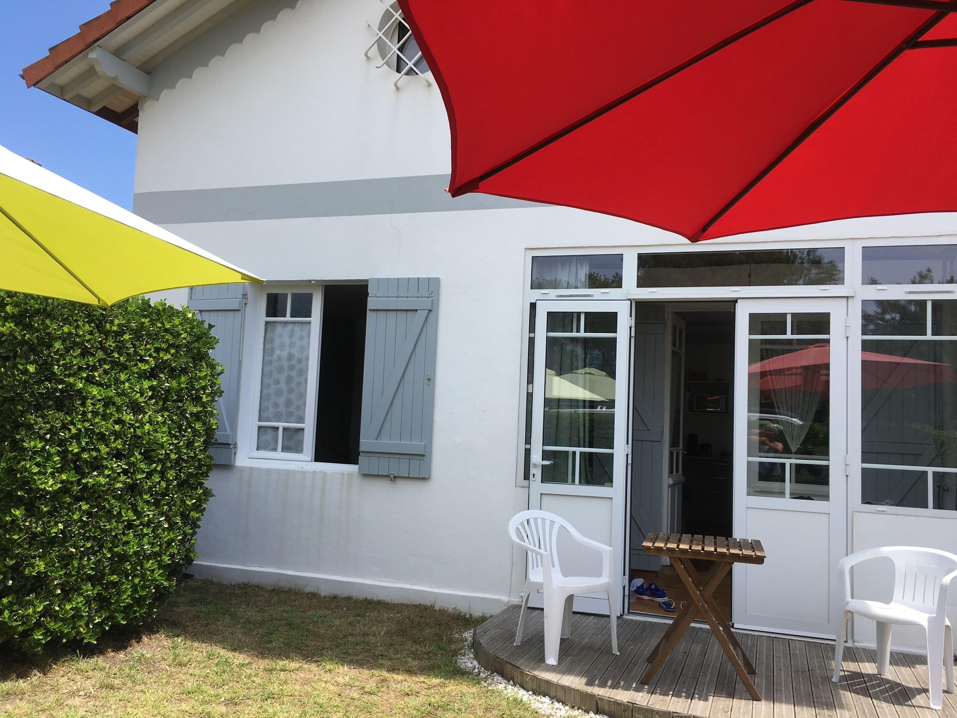 A house with a patio area featuring a wooden table and two white plastic chairs.