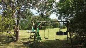A playground with swings and a slide, surrounded by trees and grass. - 17th-century farmhouse with large wooded park - quiet and charming, walking distance to town center and port (Étel)