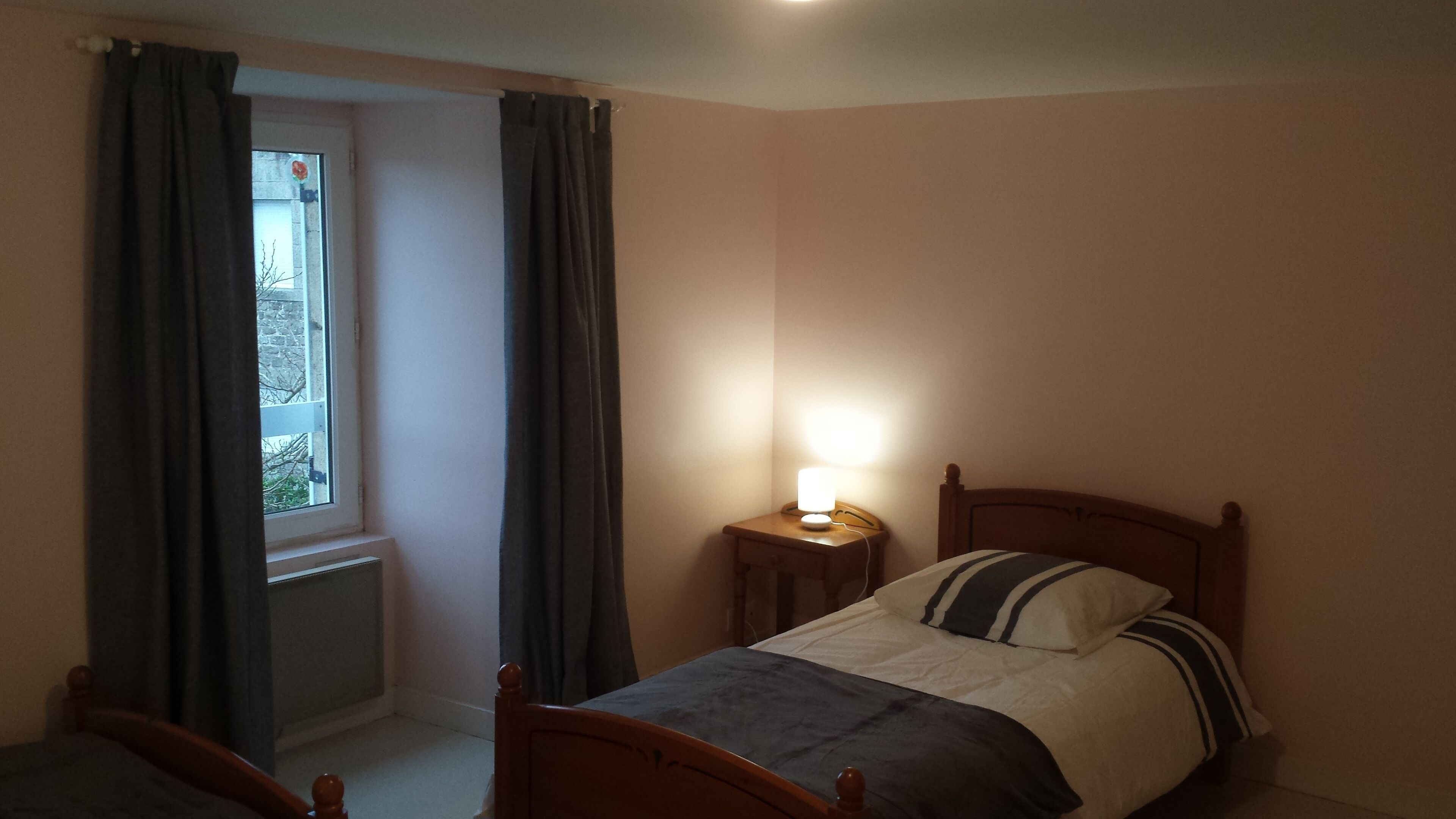 A bedroom with a bed, a bedside table with a lamp, a window with curtains, and a radiator.