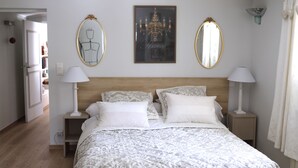 A bedroom with a wooden headboard, two bedside tables with lamps, a large bed with patterned bedding, and two wall-mounted mirrors.