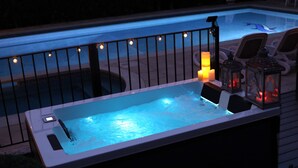 A hot tub with a railing and candles, surrounded by lounge chairs and a pool.