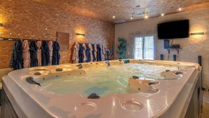 Un cuarto de spa con un jacuzzi grande, techo de madera y un televisor montado en la pared.