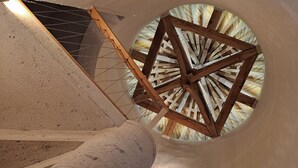 Un tragaluz circular con vigas de madera, un pilar de concreto y una puerta que da a una habitación luminosa.