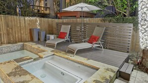 Patio con jacuzzi, dos sillas de descanso con cojines rojos, terraza de madera y cerca de madera.