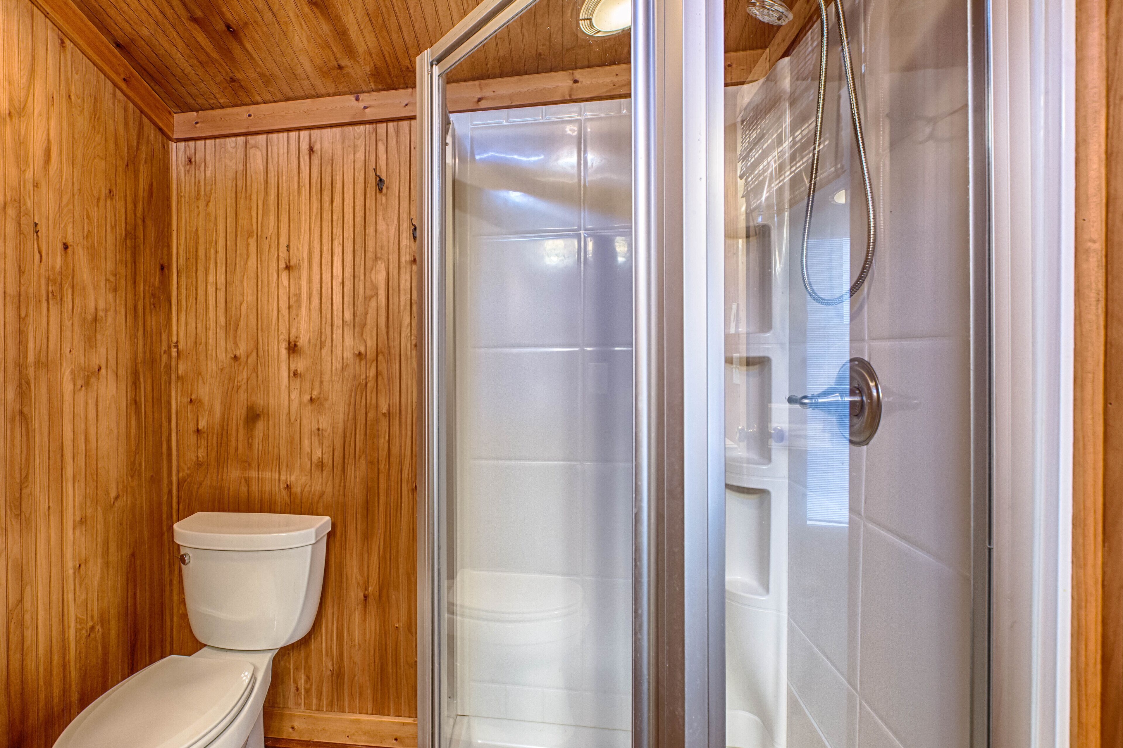 Une salle de bain aux murs lambrissés, équipée de toilettes et d’une cabine de douche en verre.