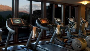 Un gimnasio con cintas de correr y elípticas, ventanas amplias con vistas a la montaña y equipo de ejercicio.