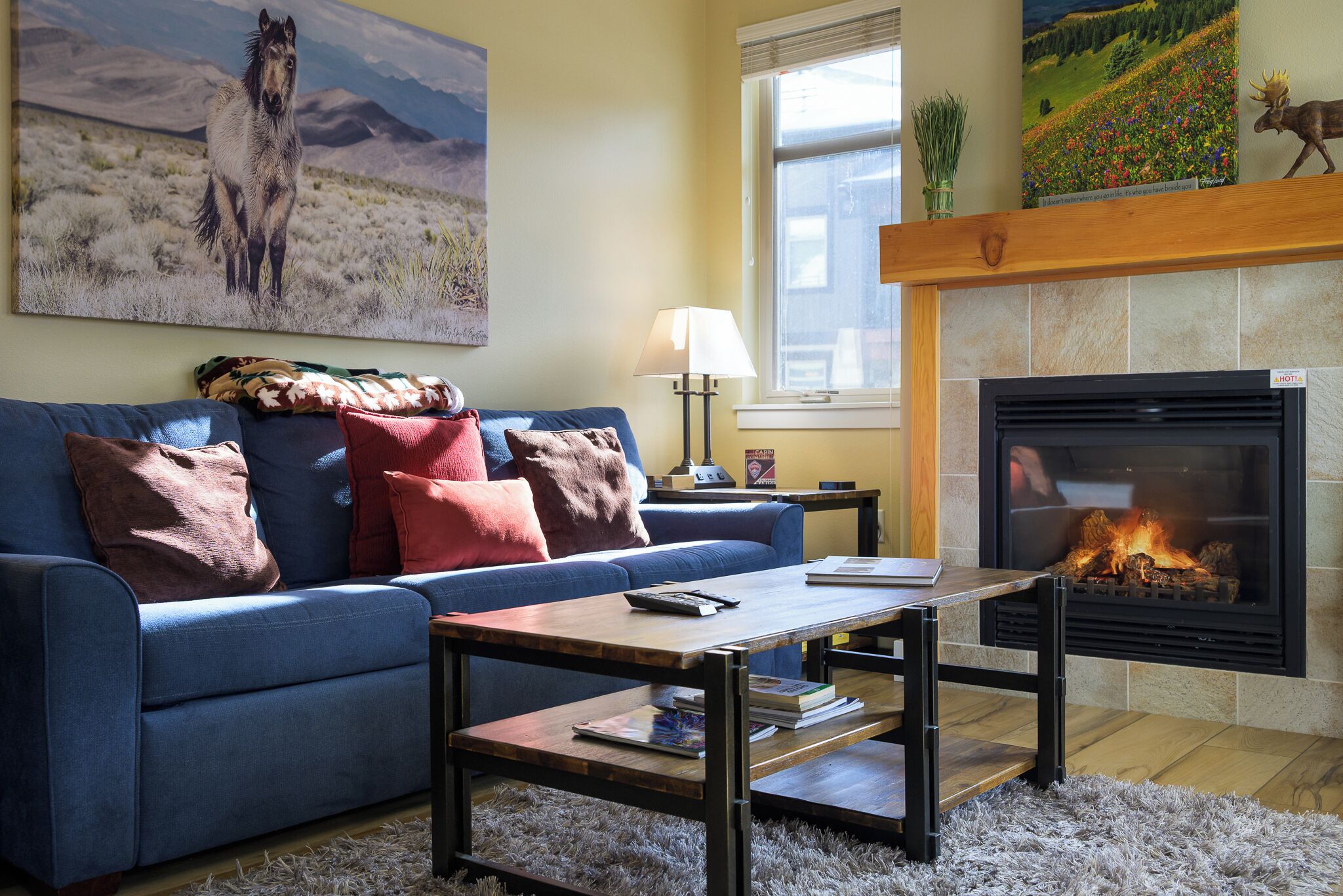 A living room with a blue sofa, a coffee table, a fireplace, and a painting of a horse.