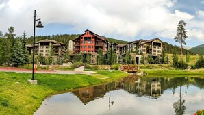 A multi-story hotel with a red facade, surrounded by greenery and a reflective pond. - Front Corner at Base: 3 King Beds, Deck, Views (Winter Park)