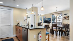 A modern kitchen with a central island, wooden cabinets, and a built-in dishwasher. There is a fire extinguisher mounted on the wall near the island. - Front Corner at Base: 3 King Beds, Deck, Views (Winter Park)