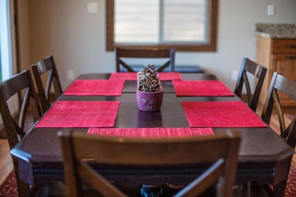 Een eettafel met rode placemats, houten stoelen en een decoratief object in het midden.