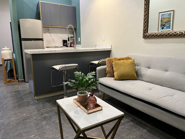 A modern kitchen with a built-in island, bar stools, and a grey sofa with a mustard throw pillow.