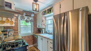 Una cocina con un refrigerador de acero inoxidable, una estufa a gas y ollas colgantes.